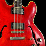 Close-up of a red electric guitar body with gold binding, dual humbucker pickups, and control knobs against a black background.