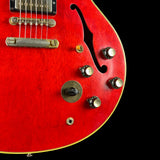 Close-up of a red electric guitar body showing the f-hole, gold-toned hardware, control knobs, and pickguard against a black background.