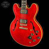 A red electric guitar with a textured red finish, gold-trimmed edges, and gold hardware, shown against a black background with a Tone Shop watermark in the top left corner.