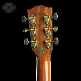 Close-up of the headstock of a Gibson electric guitar against a black background, showing six gold-toned tuning pegs and the Gibson logo near the base.