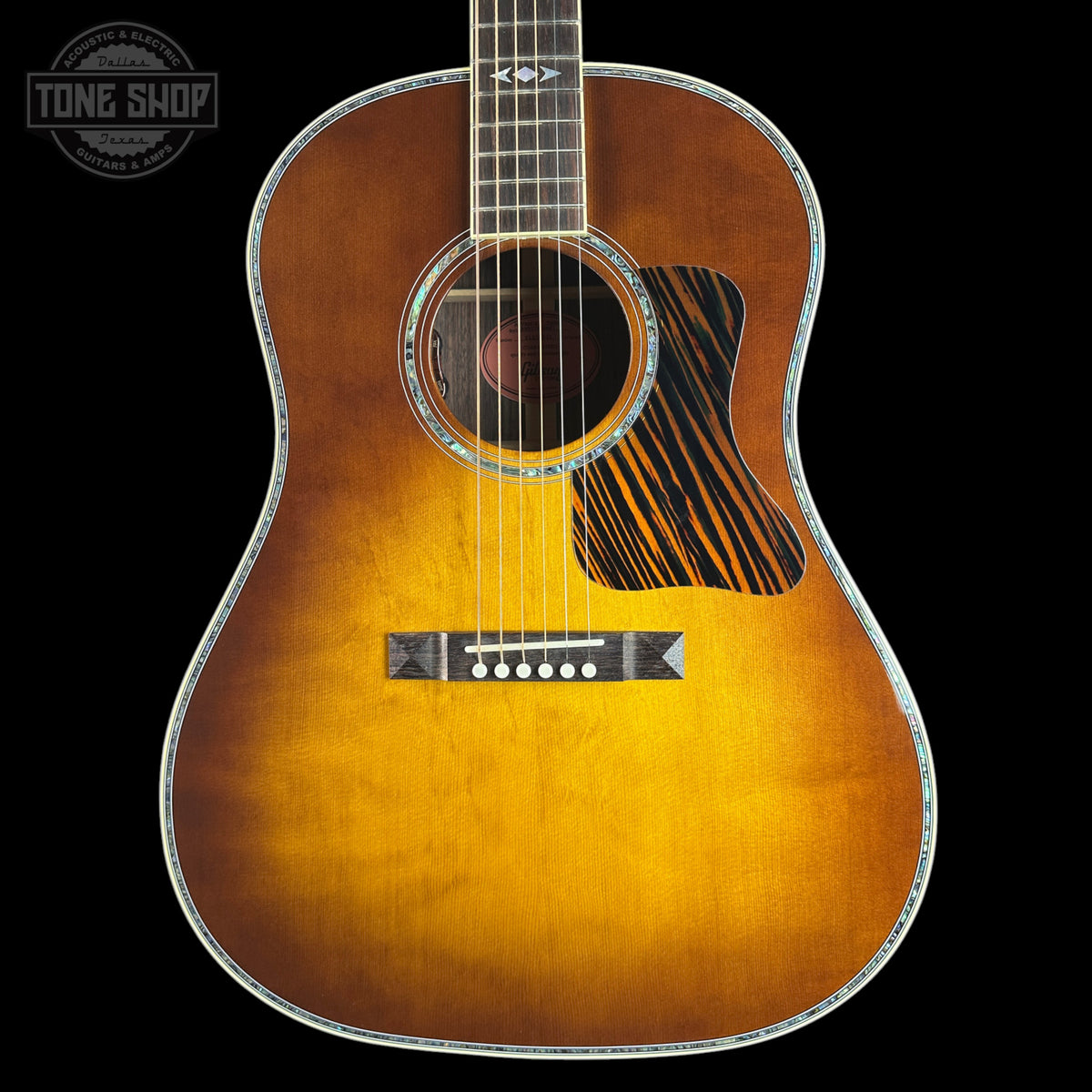 A classic acoustic guitar with a natural sunburst finish, featuring a black and brown striped pickguard and a silver-toned metal edge trim, shown against a solid black background.