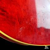 Close-up of a glossy red electric guitar body showing the wood grain, a gold edge trim, and several visible scratches on the finish against a black background.