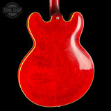 The back of a red electric guitar with a glossy finish and gold binding, shown against a black background with a Tone Shop watermark in the top left corner.