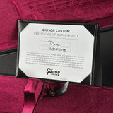 A close-up of a Gibson Custom Certificate of Authenticity card inside a black frame, placed on a deep burgundy satin ribbon and fabric background. The card is labeled for 'Dove' with serial number '23255048' and the Gibson Custom logo is visible at the bottom.