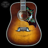 A vintage-style acoustic guitar with a natural sunburst finish, featuring intricate inlay work with a white bird, green leaves, and brown floral motifs on the upper bout. The guitar is photographed against a solid black background with a Tone Shop watermark in the top-left corner.
