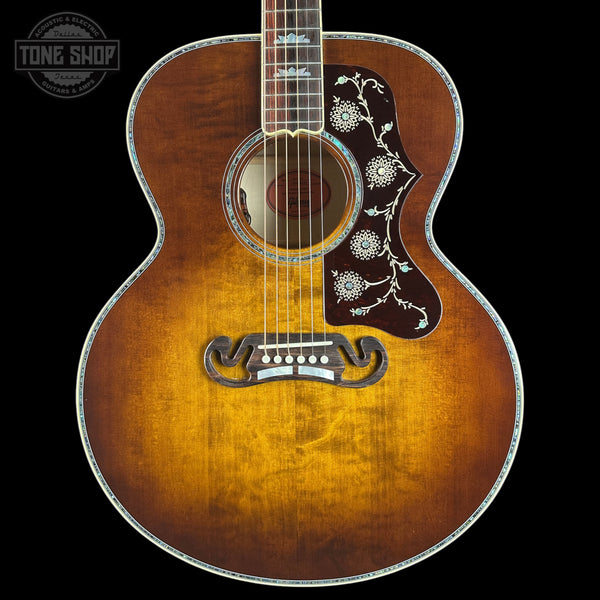 A vintage-style acoustic guitar with a sunburst finish, featuring intricate silver floral inlays on the pickguard and headstock, shown against a solid black background.