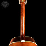 Close-up of the back of an acoustic guitar showing the rich wood grain on the back panel and neck, set against a solid black background with a Tone Shop watermark in the top left.