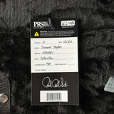 A black PRS Custom Guitars hangtag for a 'Tremolo: Stopail' model guitar, showing handwritten details, placed on a black textured fabric background.