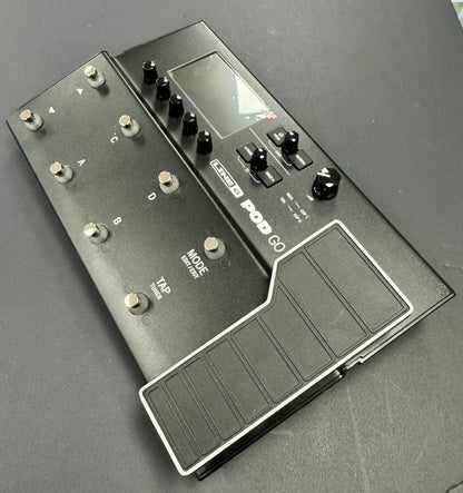 Black guitar effects pedal with multiple knobs and a footswitch on a gray background