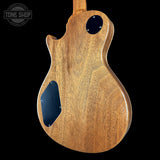 The back of an electric guitar with a natural wood finish and black pickguard, shown against a solid black background with a Tone Shop watermark in the top left corner.