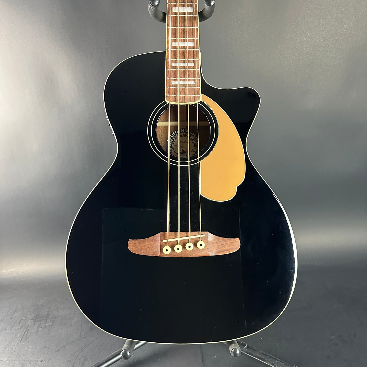 Black acoustic guitar on a stand against a gray background