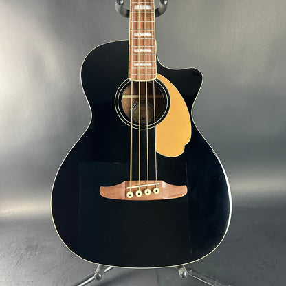 Black acoustic guitar on a stand against a gray background