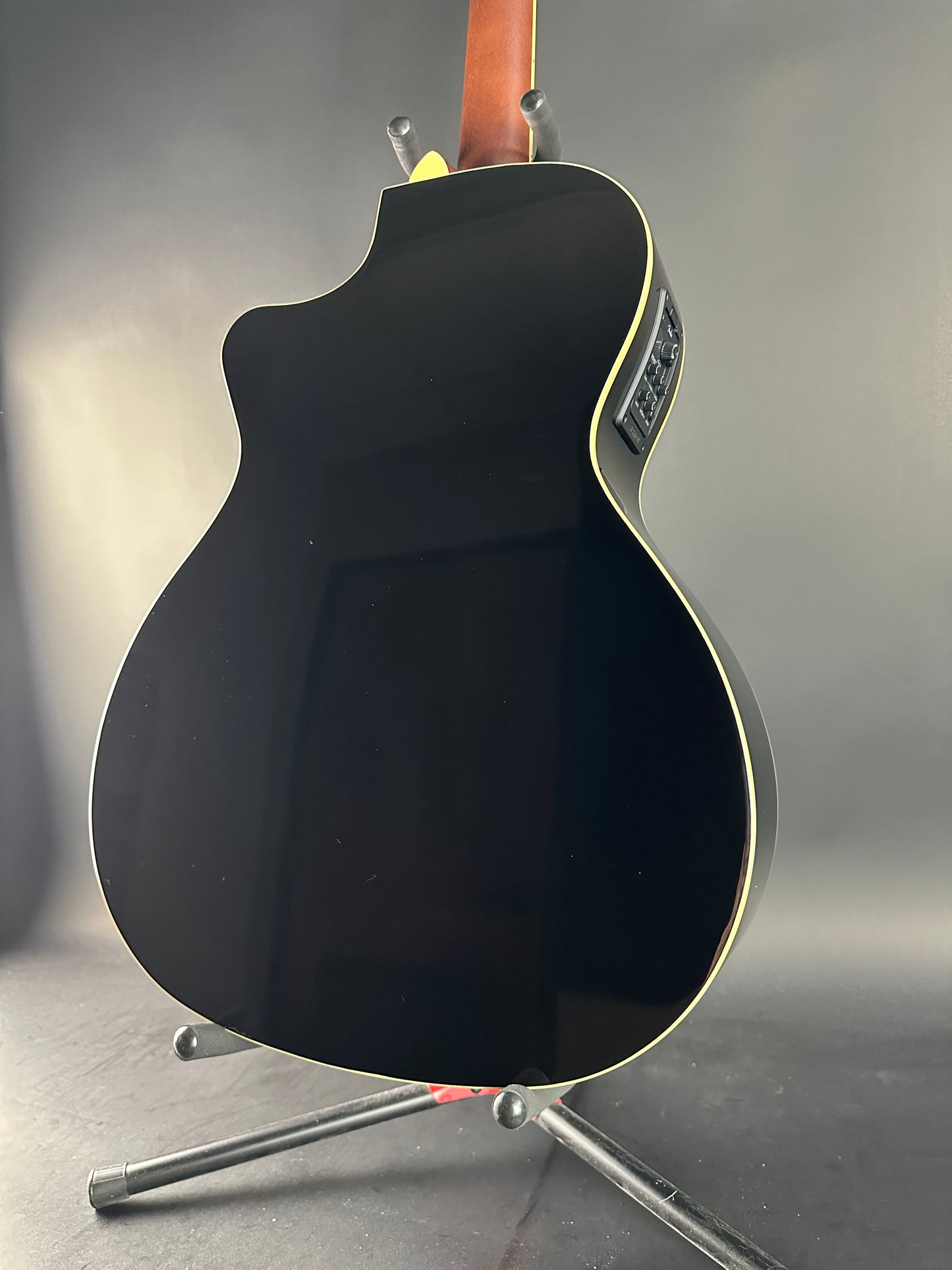 Black acoustic guitar body leaning against a gray wall