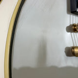 Close-up detail of a white guitar headstock or similar instrument surface, showing a cream-colored edge trim, black binding, and brass string trees.