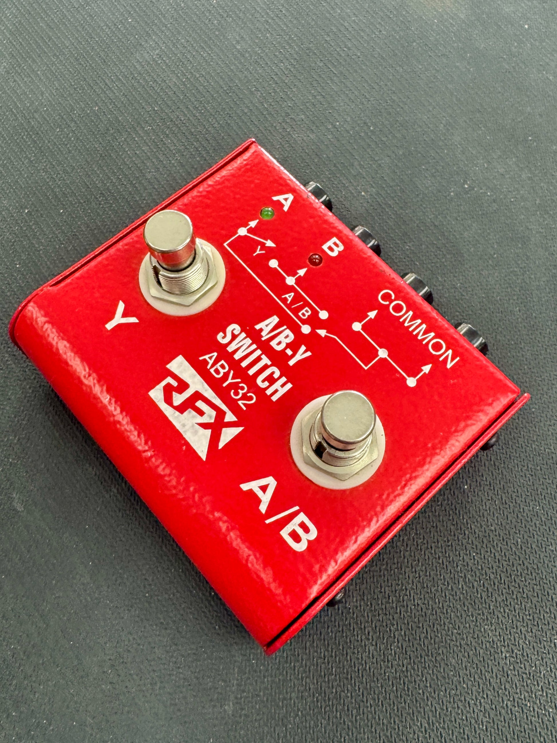 Red A/B switch pedal with brand logo on a gray background