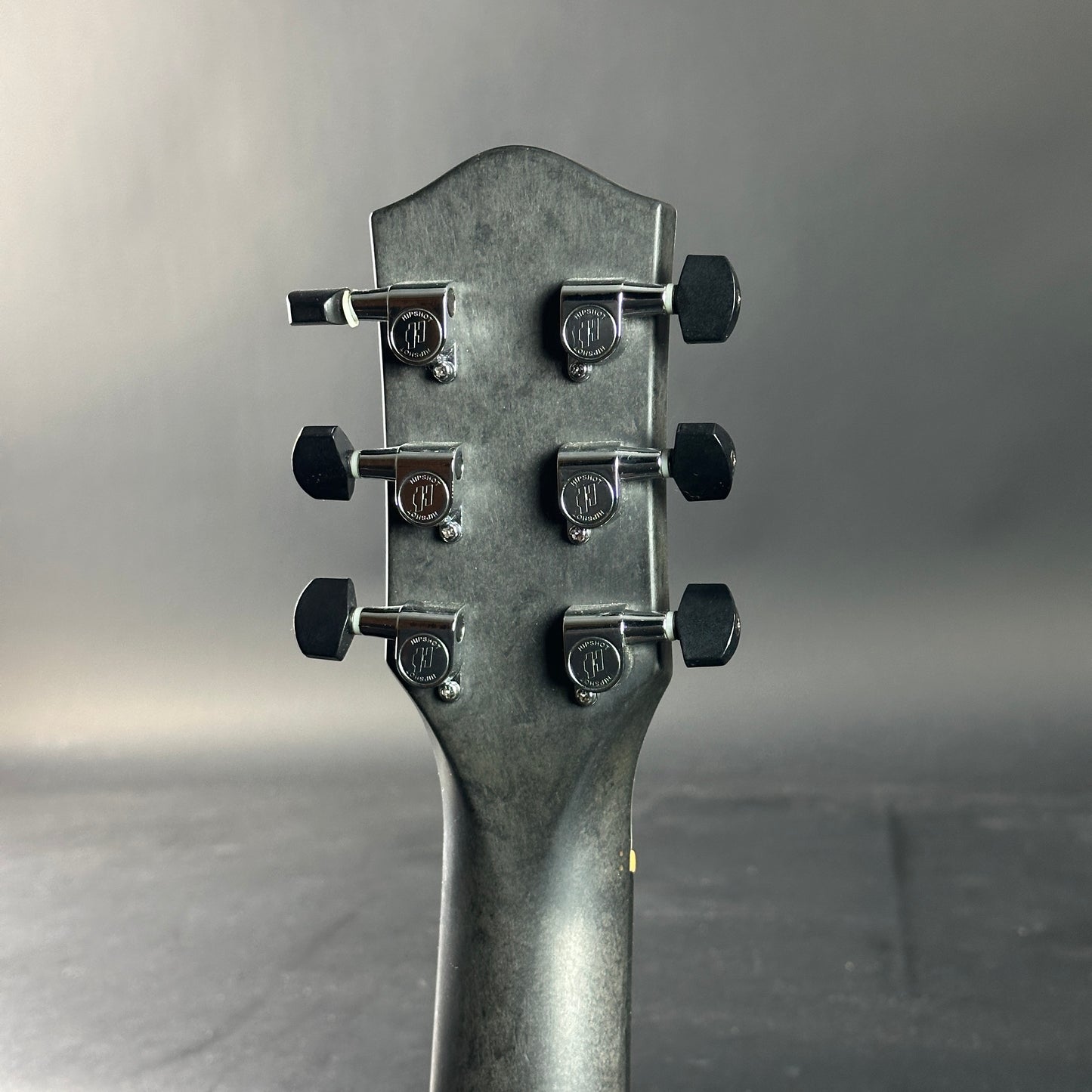 Close-up of a guitar headstock with tuning pegs on a gray background
