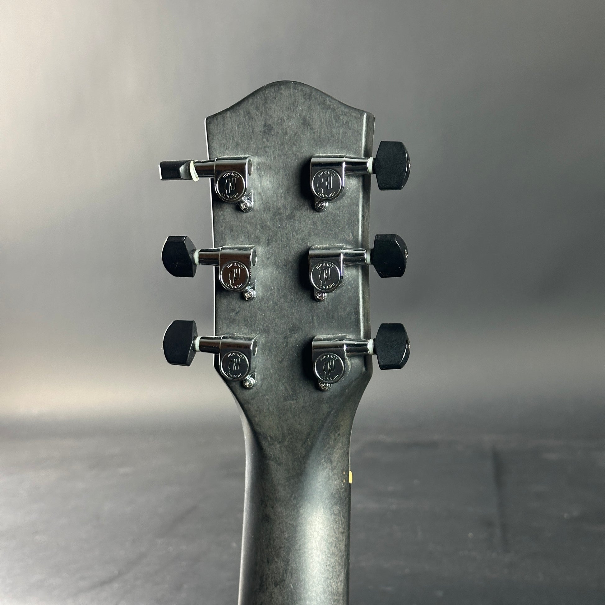 Close-up of a guitar headstock with tuning pegs on a gray background