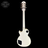 A white electric guitar shown from the back against a solid black background, featuring a white body, neck, and headstock with gold-toned tuning pegs. A circular 'TONE SHOP' watermark is visible in the top-left corner.