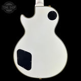 The back of a white electric guitar, likely a Gibson Les Paul Custom style, featuring a black pickguard and circular cutout, shown against a solid black background with a Tone Shop watermark in the top left.