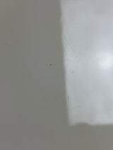 A close-up of a plain light gray or off-white surface with a soft shadow and a few faint scratches visible.