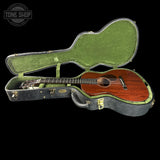 An acoustic guitar with a reddish-brown wooden body and black headstock, displayed inside an open green-lined hard case on a black background. A Tone Shop watermark is visible in the top-left corner.