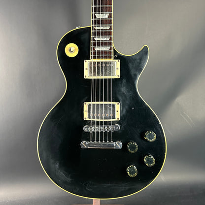Black electric guitar with gold hardware on a gray background