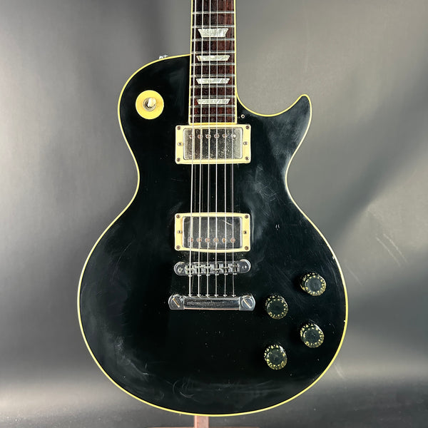 Black electric guitar with gold hardware on a gray background