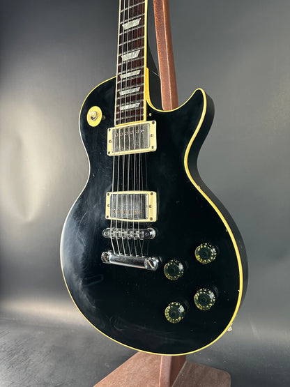 Black electric guitar with gold hardware on a gray background