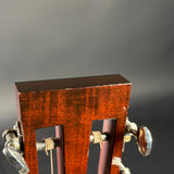 Close-up of the headstock of a guitar, showing the reddish-brown wood finish, sound holes, tuning pegs, and strings against a dark gray background.