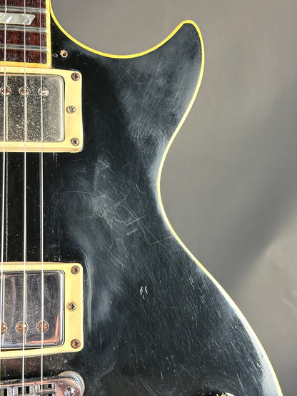 Close-up of a black electric guitar with visible wear on the body.