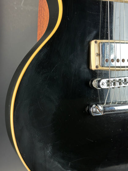 Close-up of a black electric guitar with visible wear on the body.