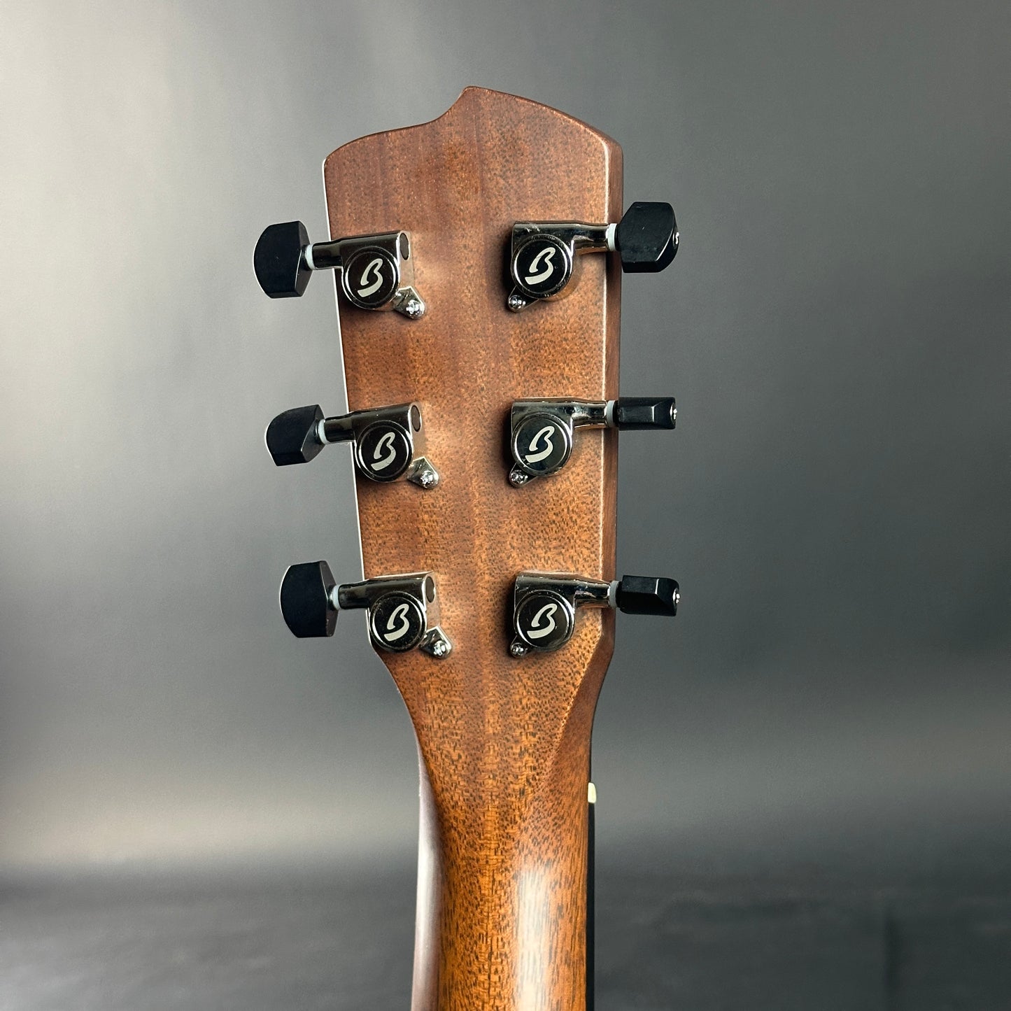 Close-up of a guitar headstock with tuning pegs on a gray background