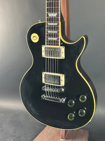Black electric guitar with gold hardware on a gray background