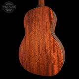 Close-up of the back of an acoustic guitar showing a rich, warm reddish-brown wood grain finish, set against a solid black background with a Tone Shop watermark in the top-left corner.