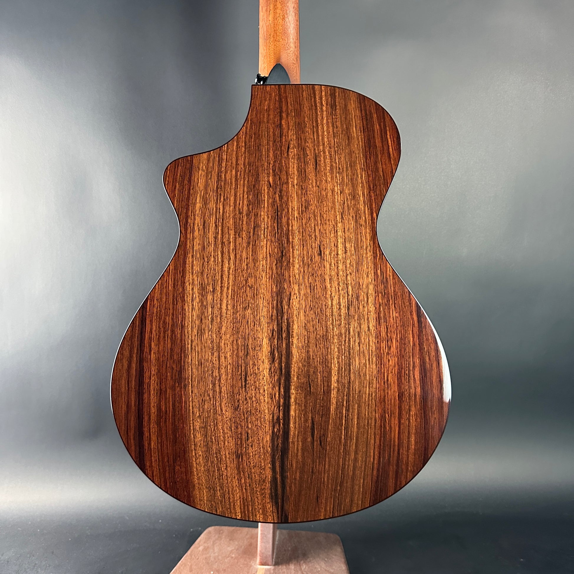 Wooden acoustic guitar body on a stand against a gray background