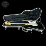 An open black hard guitar case with a black electric guitar inside, photographed against a solid black background. A Tone Shop watermark is visible in the top-left corner.