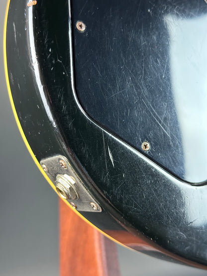 Close-up of a guitar's black pickguard with visible scratches and a metal plate.