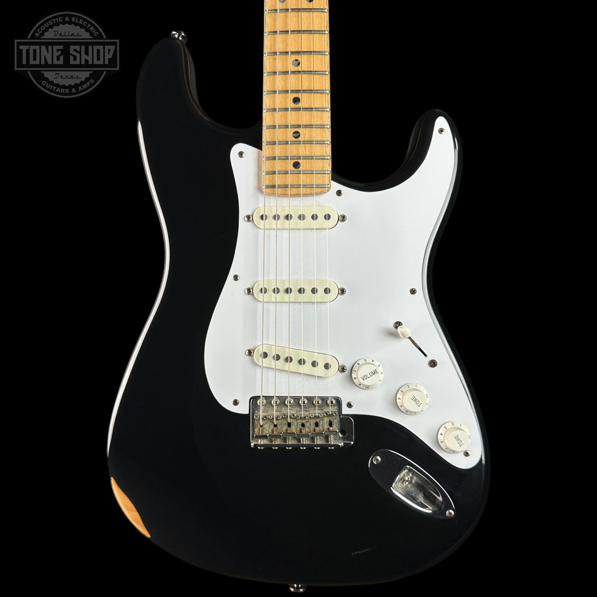A black electric guitar with a white pickguard and maple neck, photographed against a solid black background. A Tone Shop watermark is visible in the top-left corner.