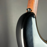 Close-up detail of a glossy black electric guitar body with a visible wood neck and a silver hardware knob against a neutral gray background.
