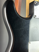 Close-up of a black electric guitar body with a silver pickguard and visible scratches on the glossy finish.
