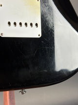 Close-up of the rear side of a glossy black electric guitar body with visible scratches, a white pickguard, and a silver control screw.