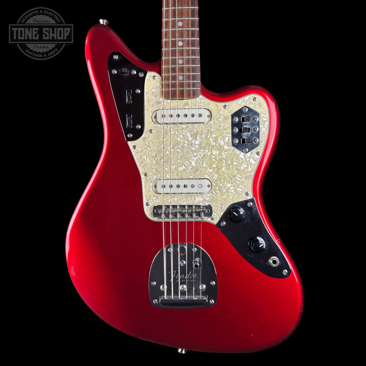 A red electric guitar with a cream pearlescent pickguard and black control plates, shown against a black background with a Tone Shop watermark in the top left corner.