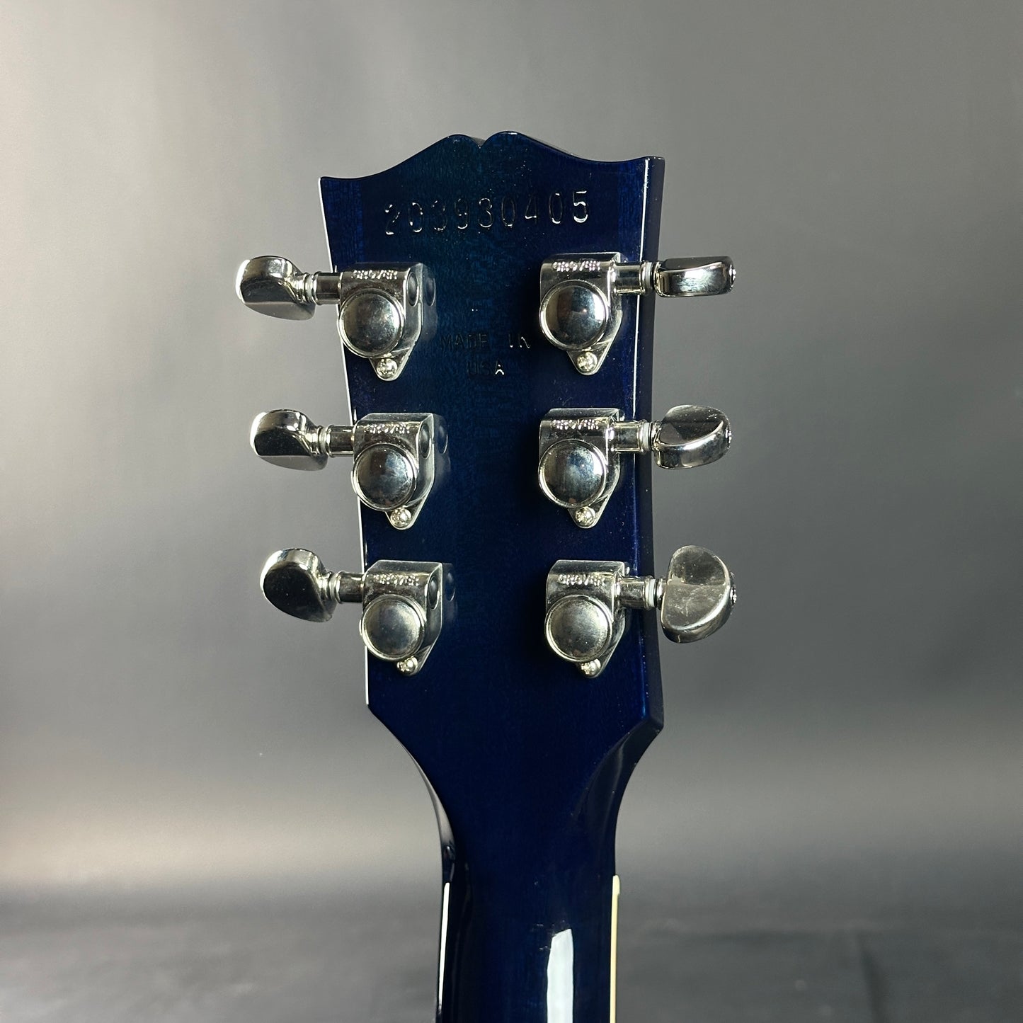 Close-up of a blue guitar headstock with tuning pegs on a gray background