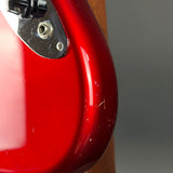 Close-up of a glossy red electric guitar body showing the edge of the body, a chrome hardware plate, and part of a black control knob against a neutral gray background.