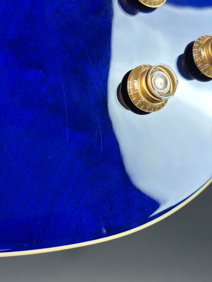 Close-up of a blue guitar with gold hardware on a gray background