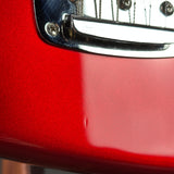 Close-up of a glossy red electric guitar body with a chrome hardware piece and part of a silver pickguard visible.