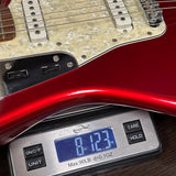 A close-up of a red electric guitar body resting on a digital scale, showing the scale reading 8.123 oz.