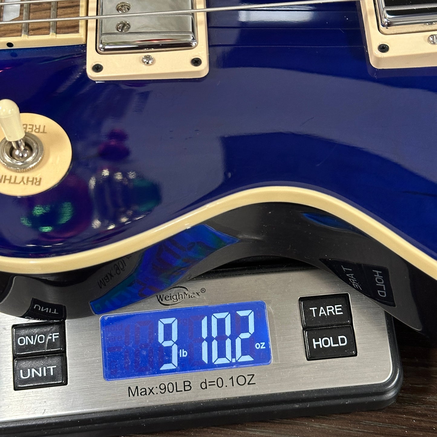 Blue electric guitar on a digital scale displaying weight.