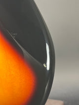 Close-up of a glossy black curved surface with a warm orange-brown gradient visible in the lower right, against a neutral gray background.
