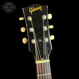 Close-up of a Gibson acoustic guitar headstock with six cream-colored tuning pegs and a black finish, set against a solid black background. A Tone Shop watermark is visible in the upper left corner.